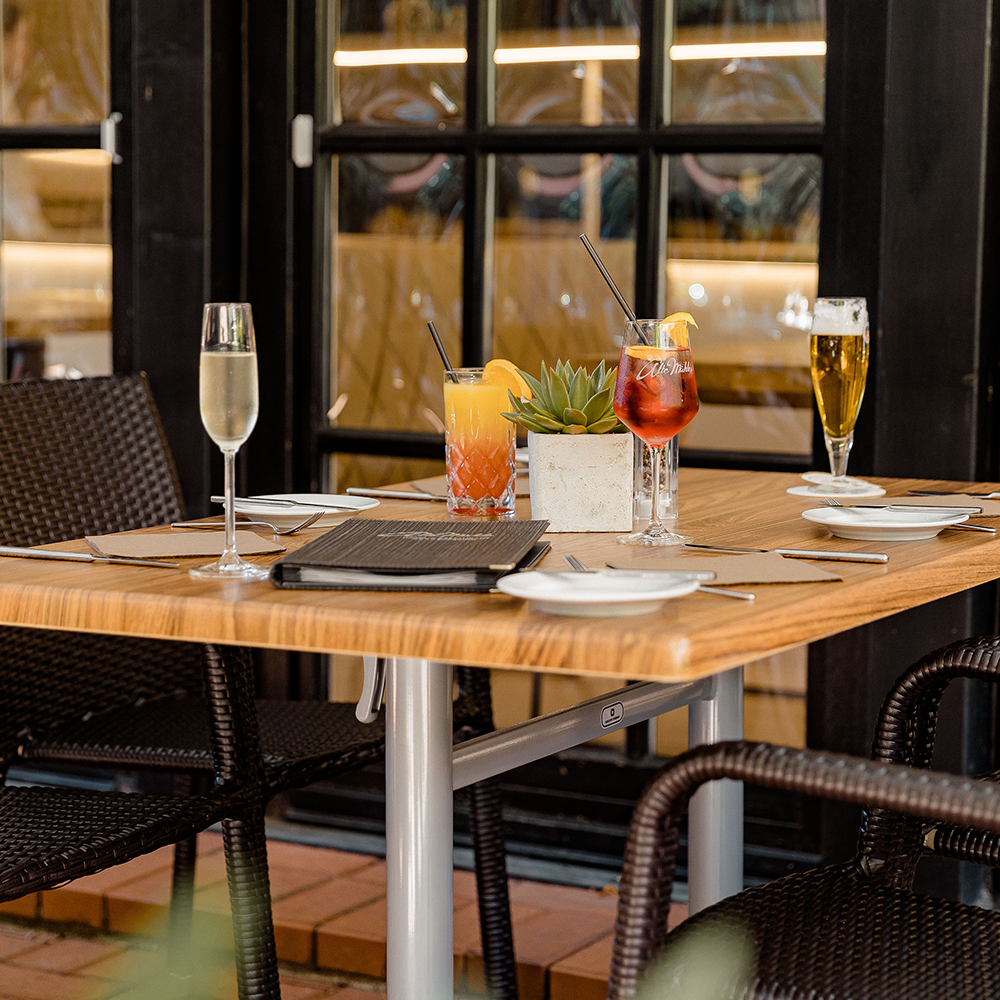 Tisch im Restaurant Alte Mühle mit vier Getränken: Sekt, zwei Cocktails und Bier, dazu Besteck und Servietten.