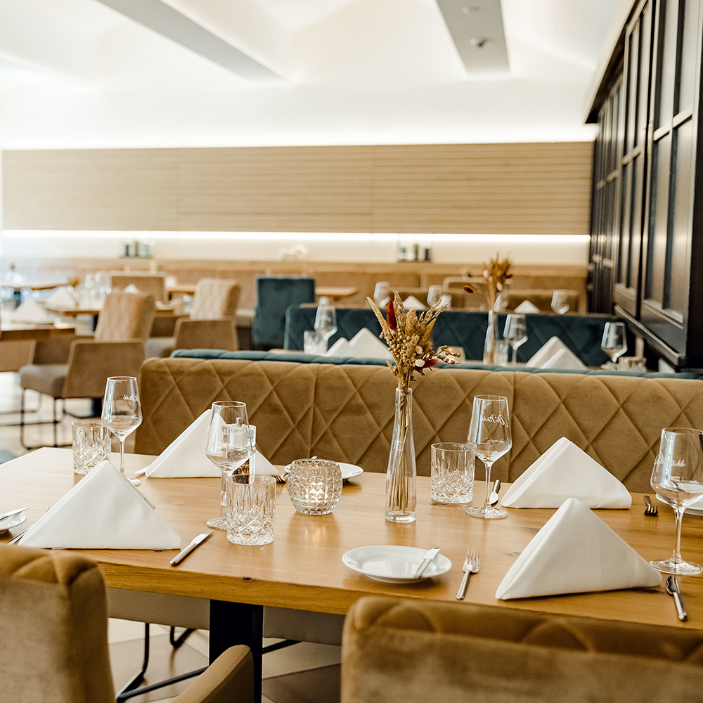 Elegantes Restaurant mit gedeckten Tischen, weißen Stoffservietten, Kristallgläsern und getrockneten Blumen in Vase